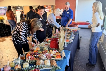 People serving themselves from a buffet table with assorted food items at an indoor event.