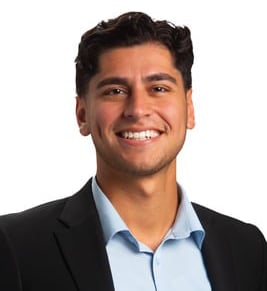 A male business consultant wearing a blue blazer, checkered shirt, and smiling, with short brown hair.